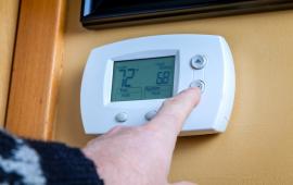 Person pushing a button on a smart thermostat controller 
