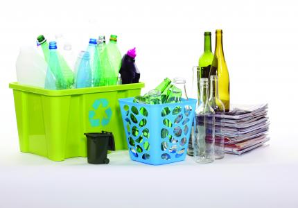 An assortment of recyclable materials including plastic and glass bottles and newspapers in various recyclable storage bins