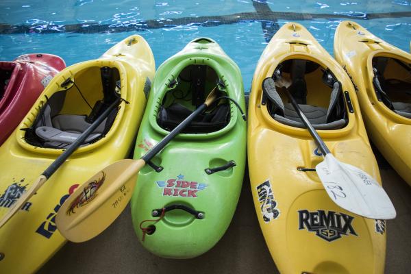 Empty kayaks with paddles lined up next to the Aquatic Center Pool